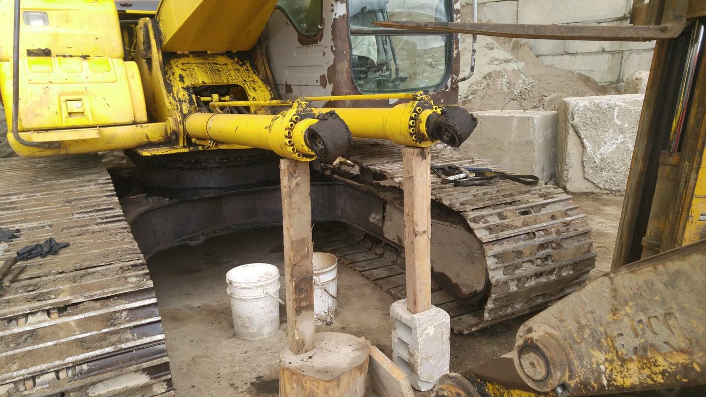 Large excavator hydraulic cylinder removed and supported on cribbing for service